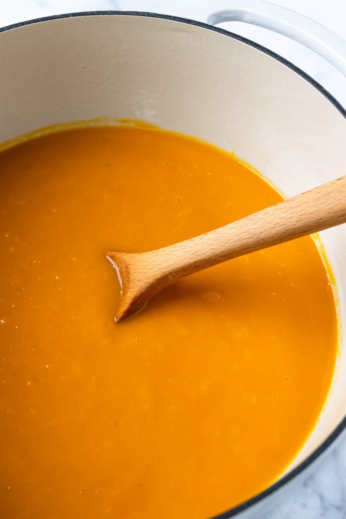 Closeup of Honeynut Squash Soup in a pot with a Wooden Spoon.