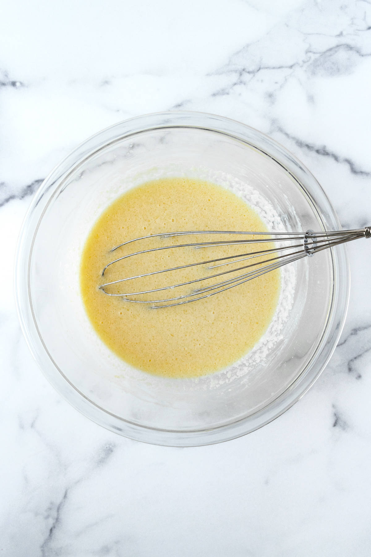 Cornbread wet ingredients in a glass bowl with a whisk.