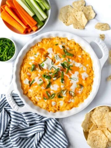 Greek Yogurt Buffalo Chicken Dip in a White Dish on a countertop with chips and veggies for dipping.