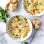 Creamy Orzo Chicken Soup in 2 white bowls on a marble countertop with fresh bread.