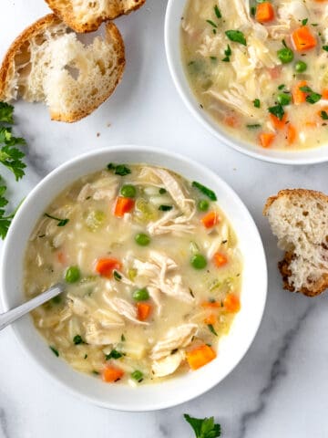Creamy Orzo Chicken Soup in 2 white bowls on a marble countertop with fresh bread.