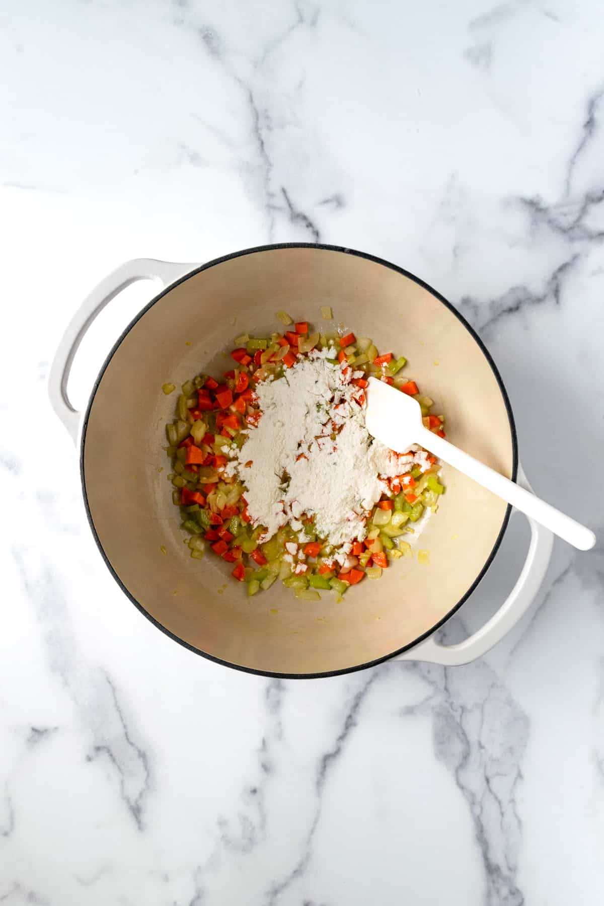 Carrots Celery Onion and Garlic with Flour in a White Dutch Oven.
