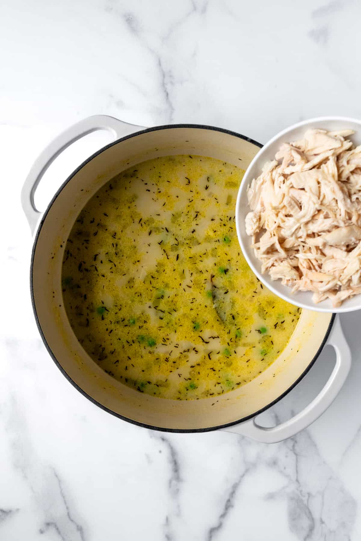 Adding shredded chicken to creamy orzo chicken soup.