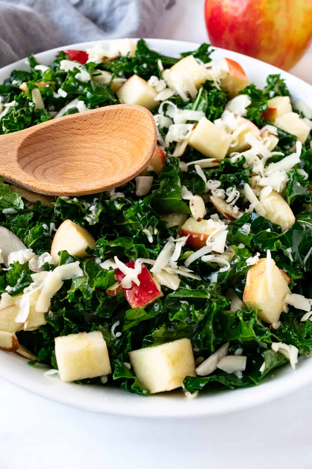 Kale Salad with Apples and Cheddar with a wooden serving spoon.