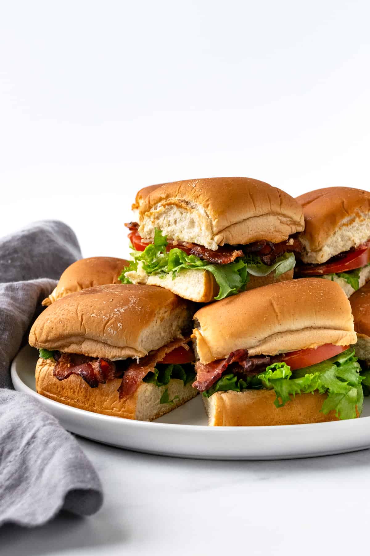 BLT Sliders stacked on a white serving plate.