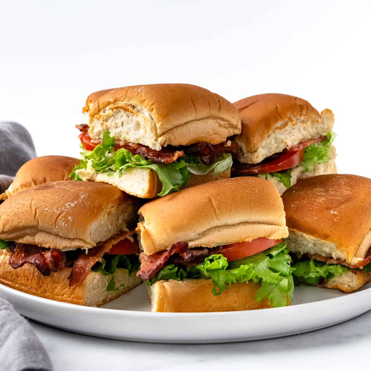 BLT Sliders stacked on a white serving plate with a white background.