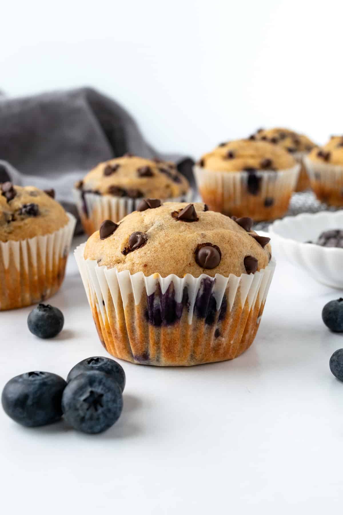 Blueberry Chocolate Chip Muffins on a marble countertop with fresh blueberries and mini chocolate chips scattered around.