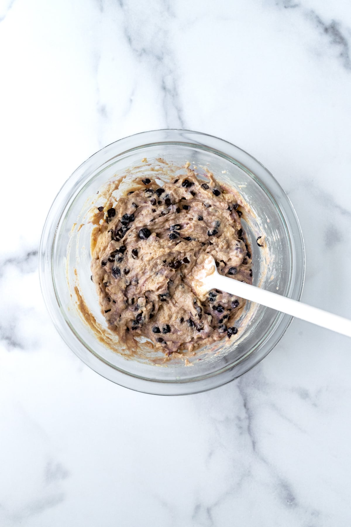 Blueberry Chocolate Chip Muffin Batter in a clear bowl with a white spatula.