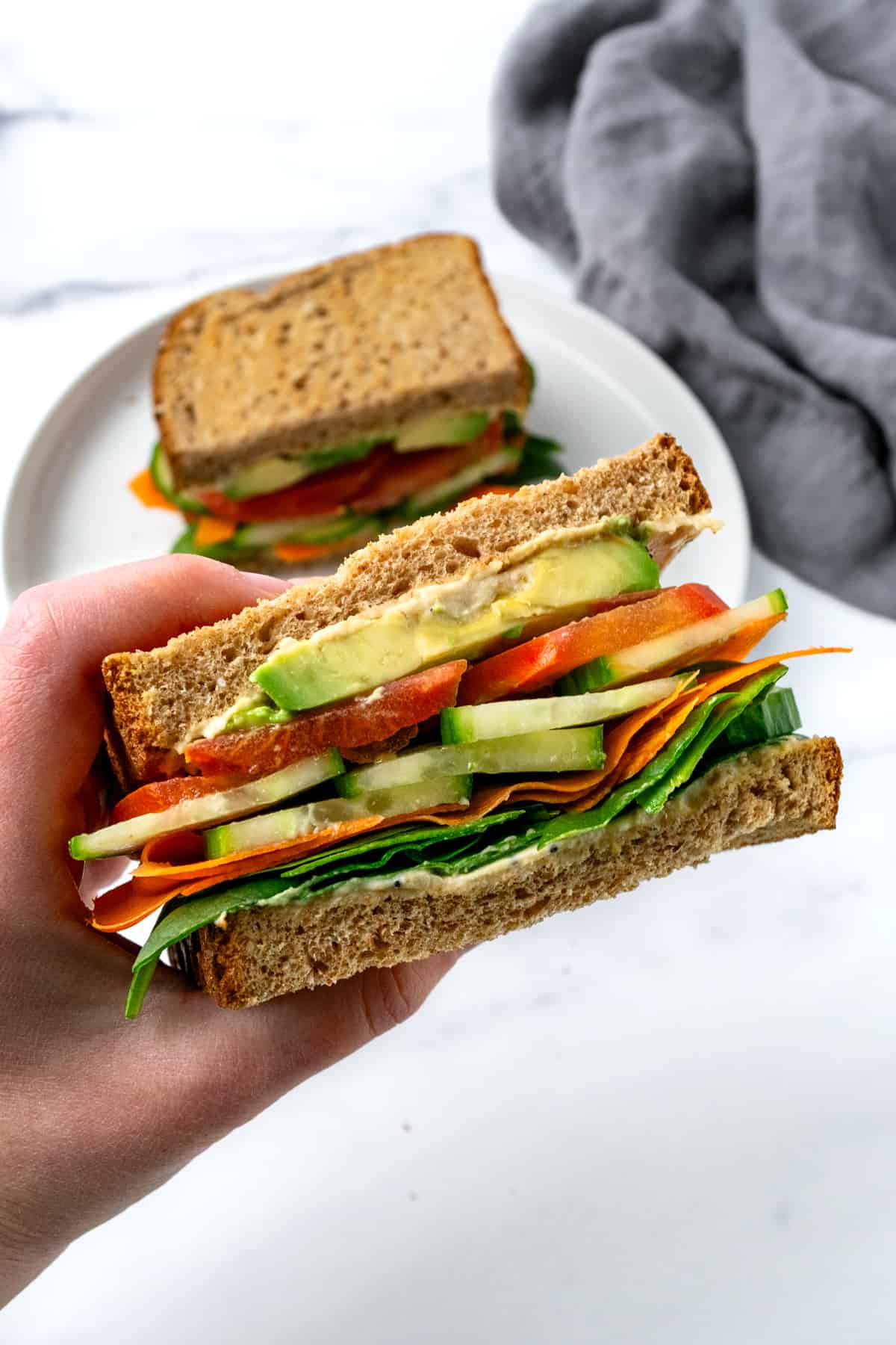 A hand holding a half of a cucumber hummus sandwich with veggie toppings.