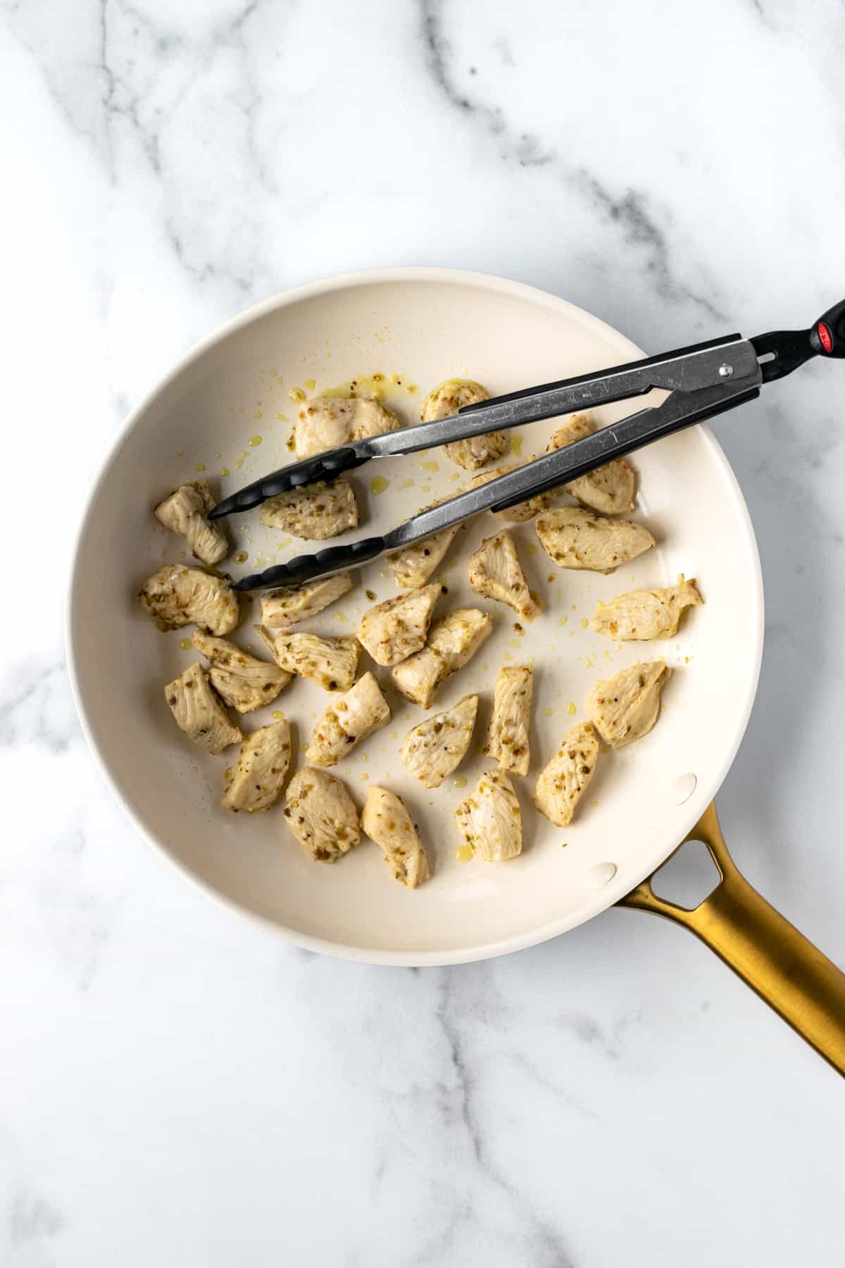 Mediterranean Chicken in a white skillet with tongs.