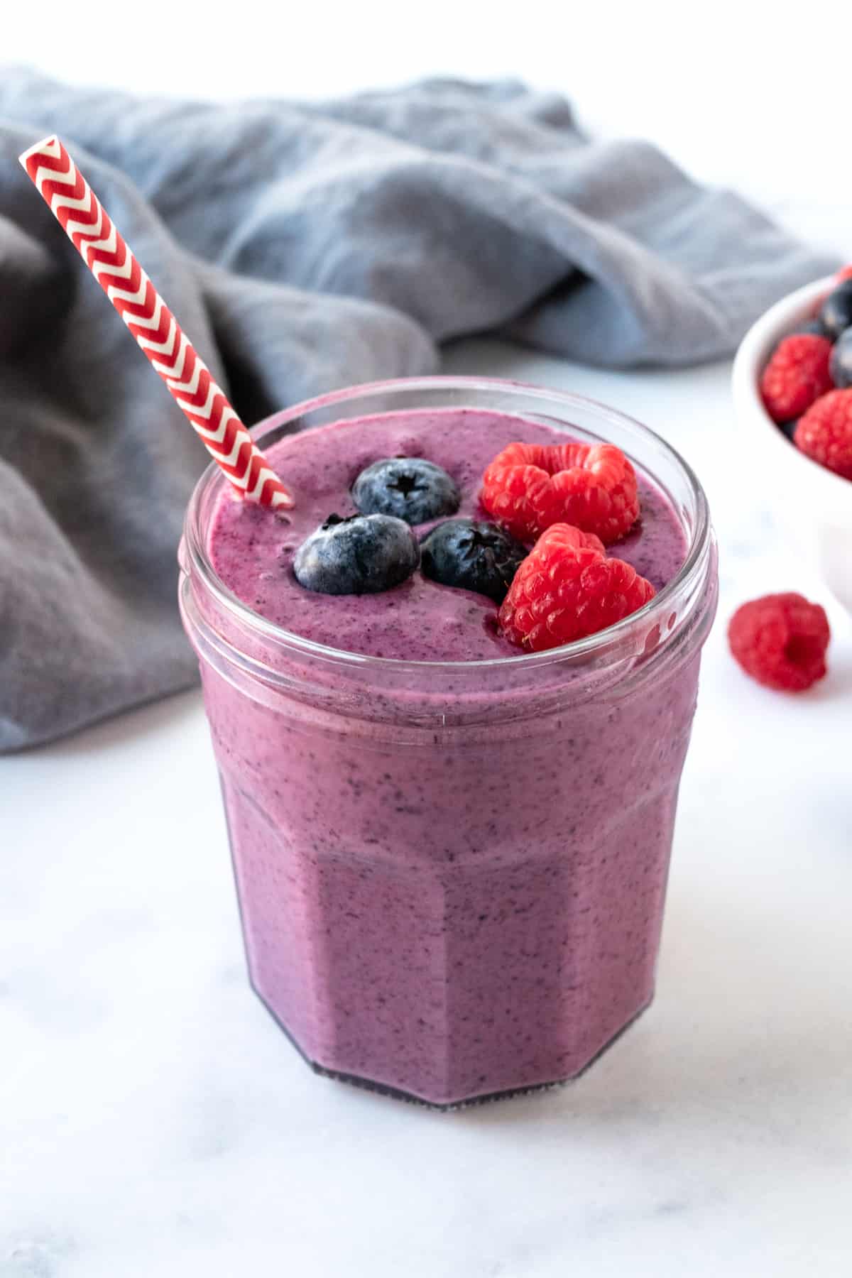 Raspberry Blueberry Smoothie in a glass topped with fresh blueberries and raspberries.