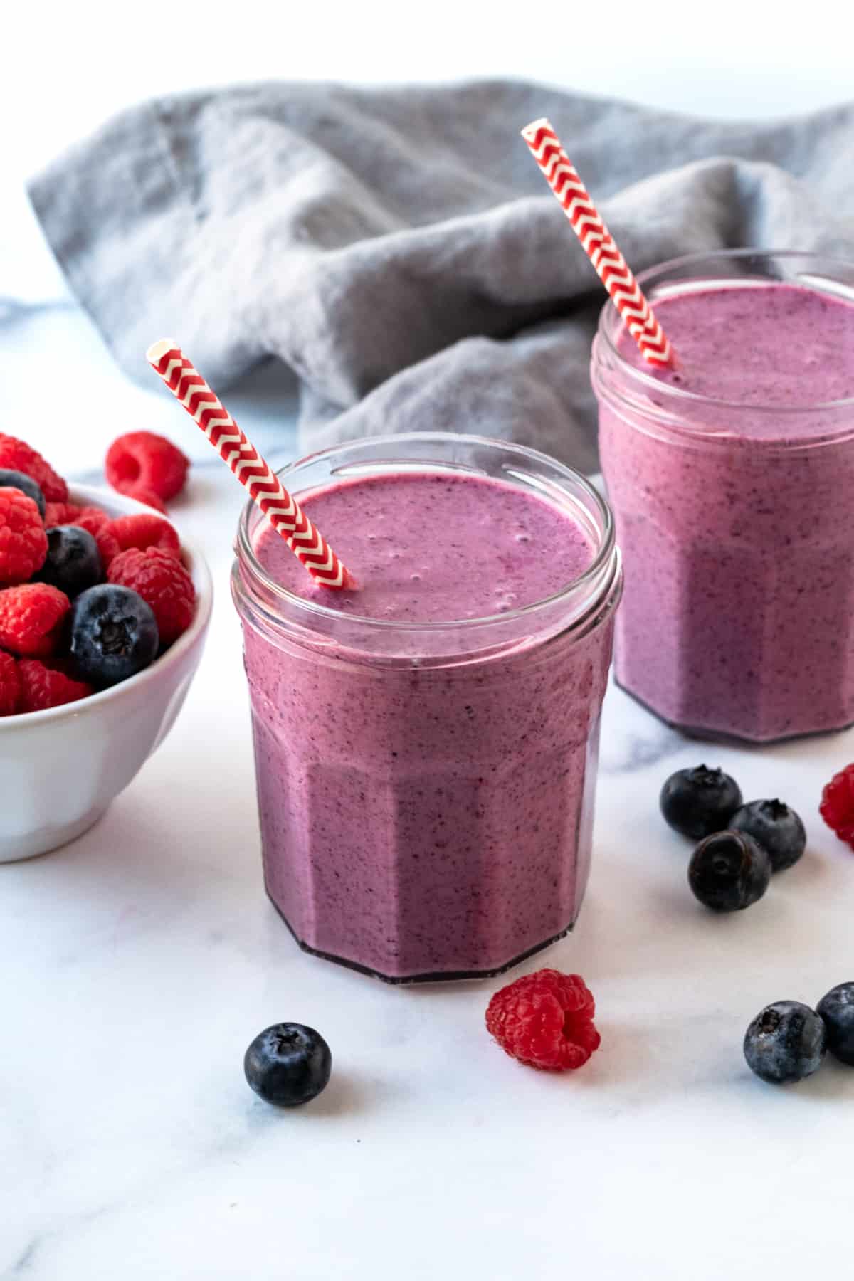 Two blueberry raspberry smoothies in glasses with straws.