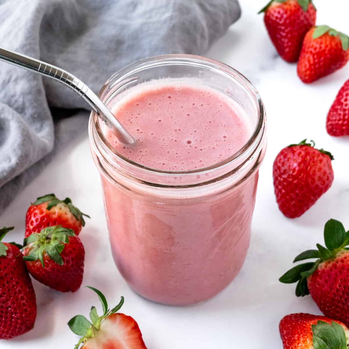 Almond Milk Strawberry Smoothie in a glass with a metal straw on a marble countertop.