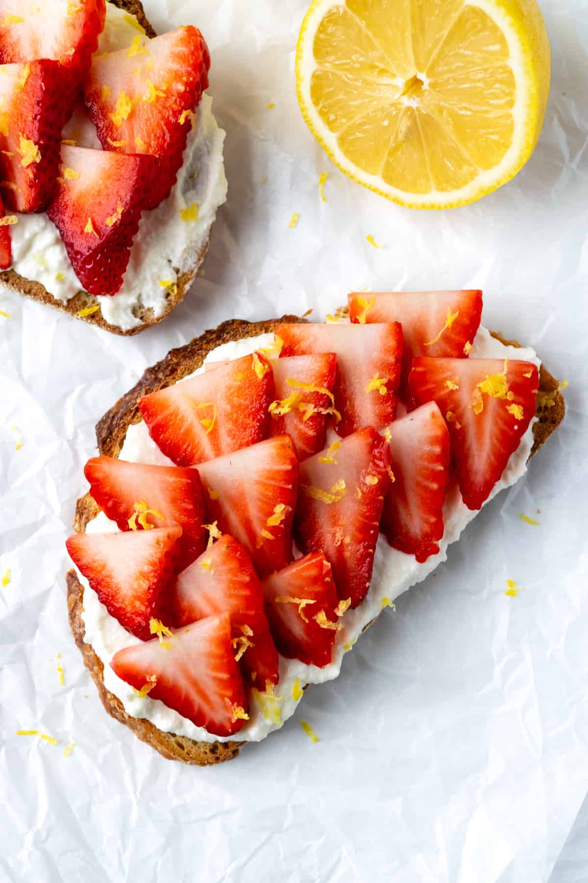 Strawberry Ricotta Toast on parchment paper with a lemon.