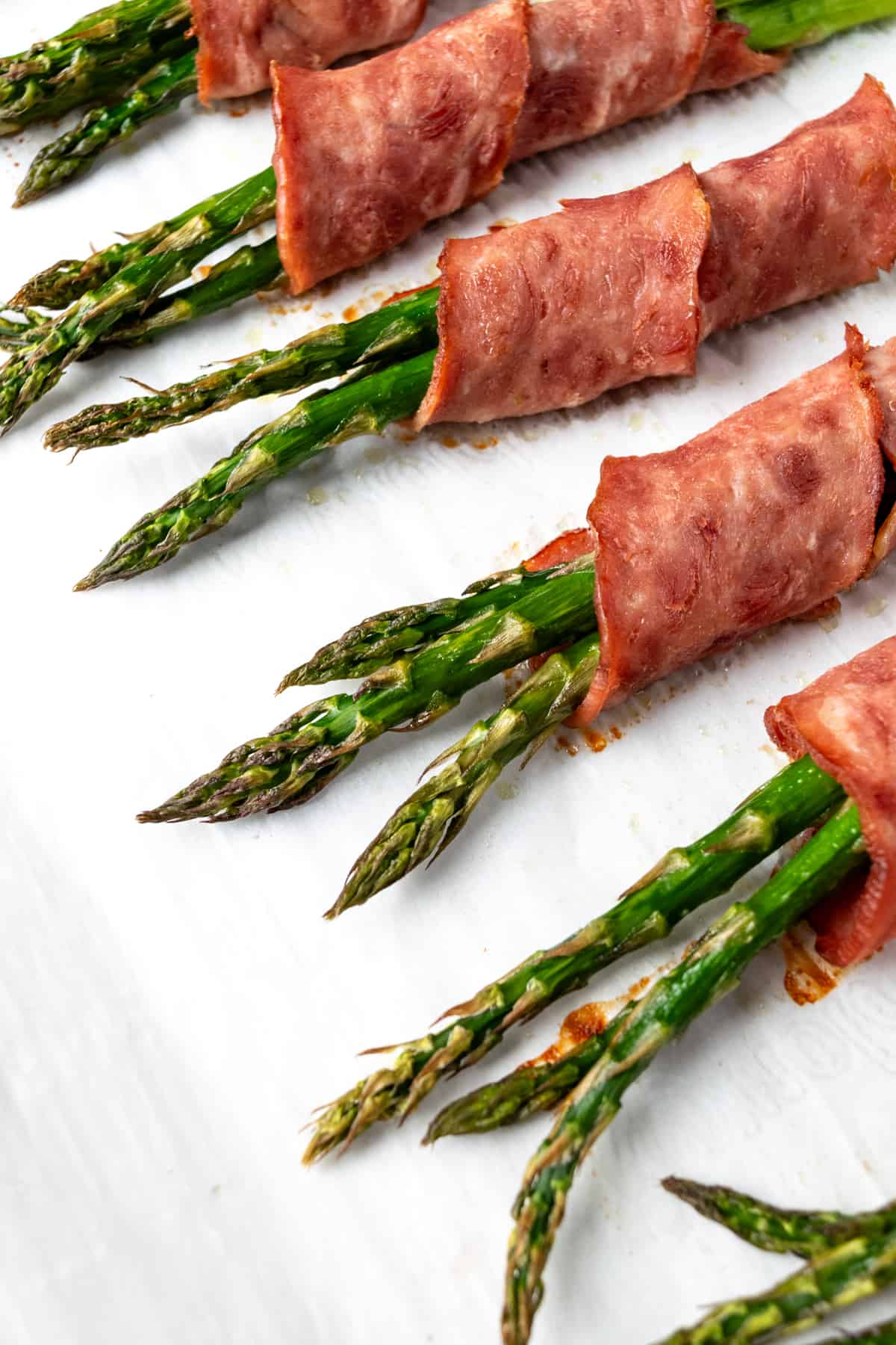 Baked Turkey Bacon Wrapped Asparagus on a piece of white parchment paper.