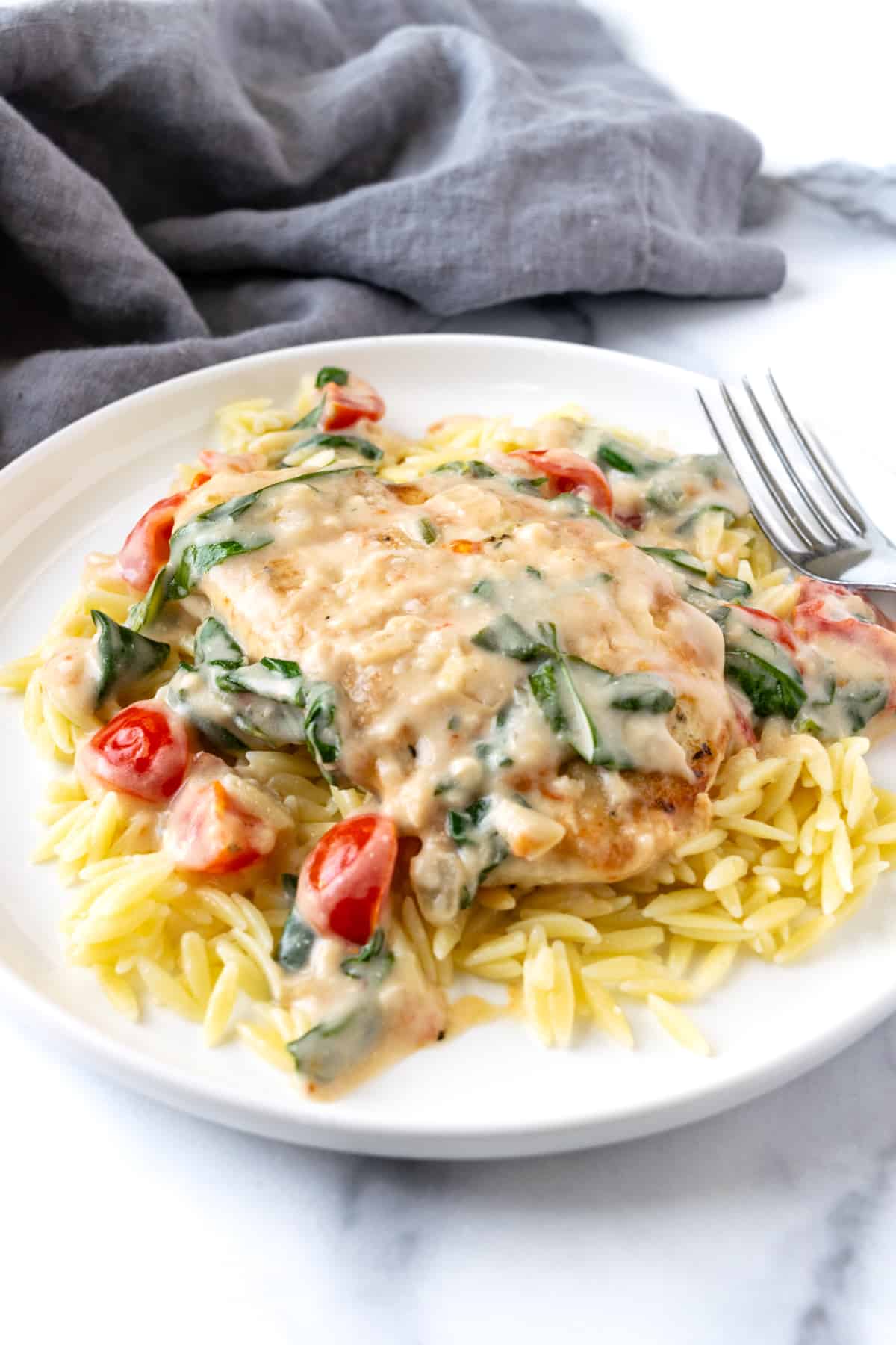 Creamy Chicken Florentine with Tomatoes over orzo on a white plate.