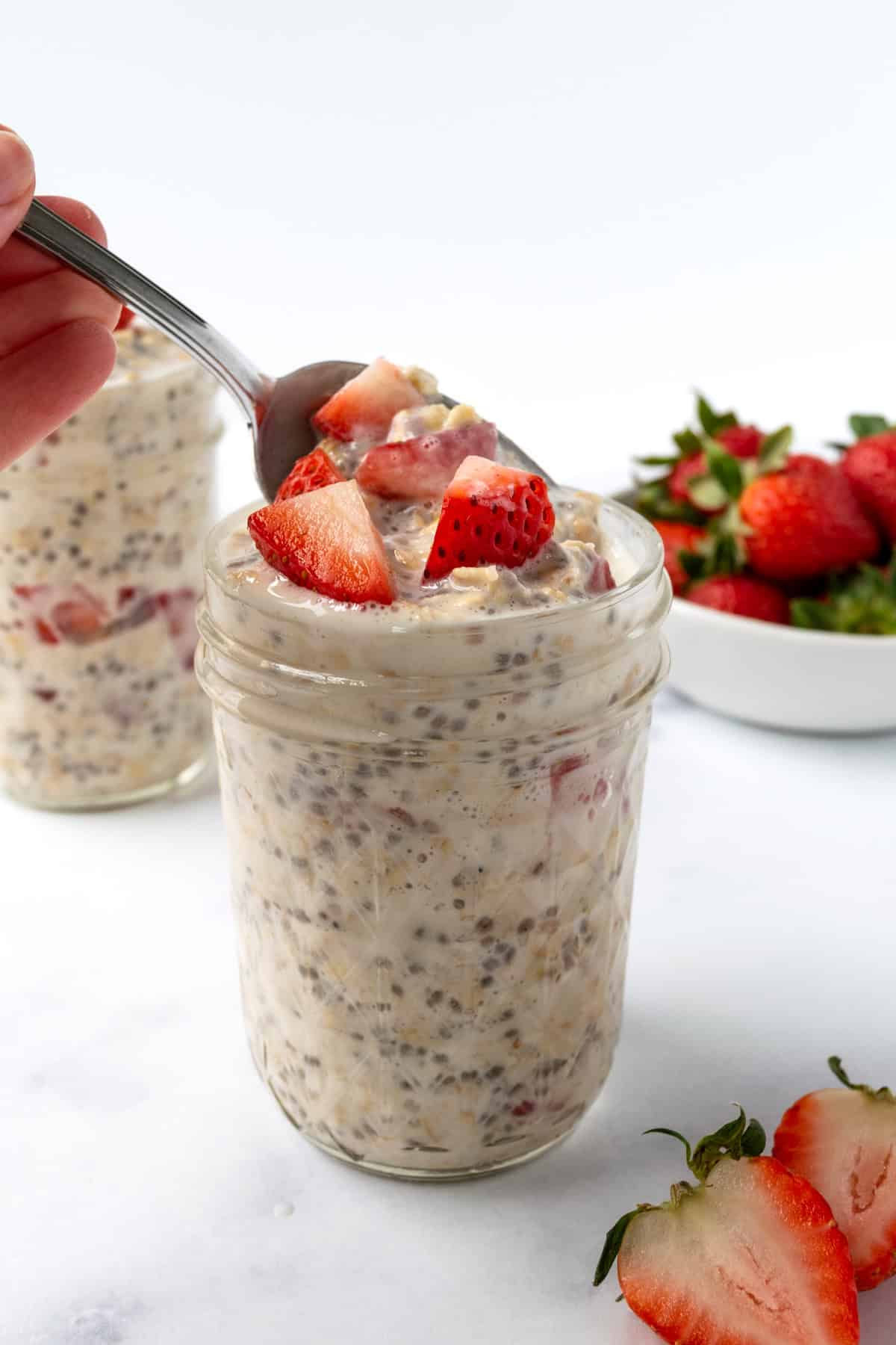 A spoon taking a scoop of strawberry overnight oats from a glass jar.