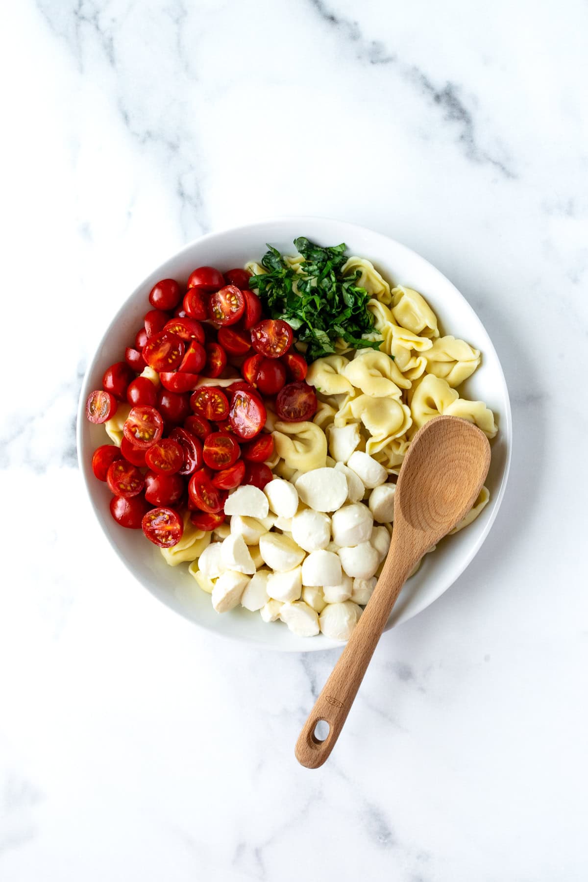 Tortellini Caprese Salad in a white bowl with a spoon before mixing.