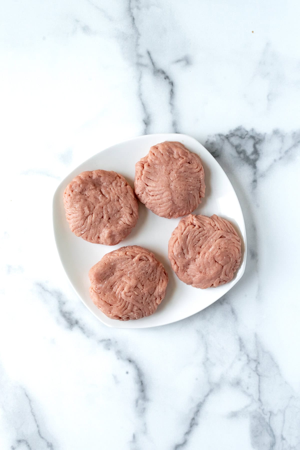 Raw Turkey Burgers on a White Plate.