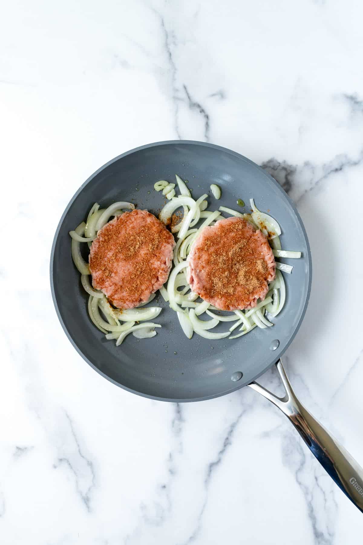 Two Smashed Turkey Burgers Over Sliced Onions in a Skillet.
