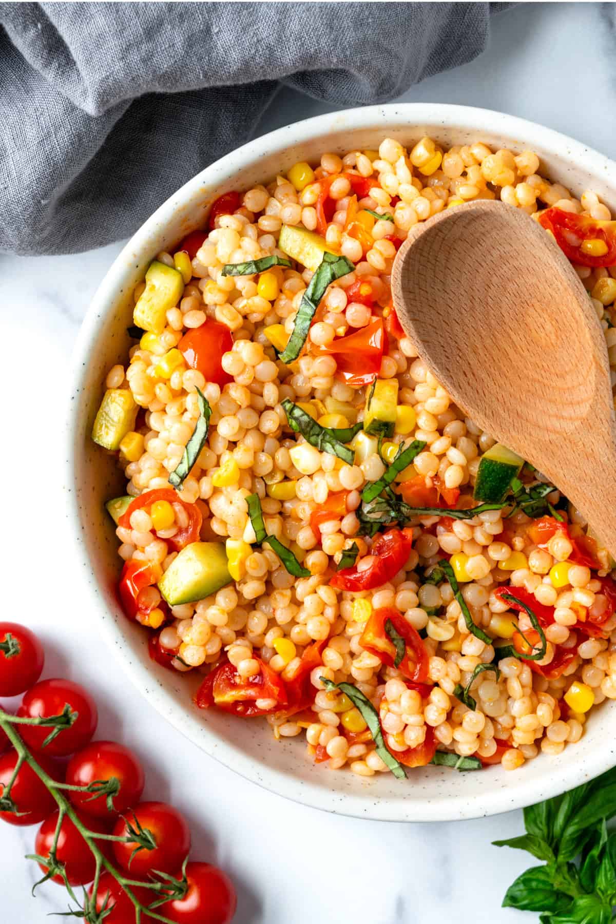 Summer Couscous Salad in a white bowl with a wooden serving spoon.