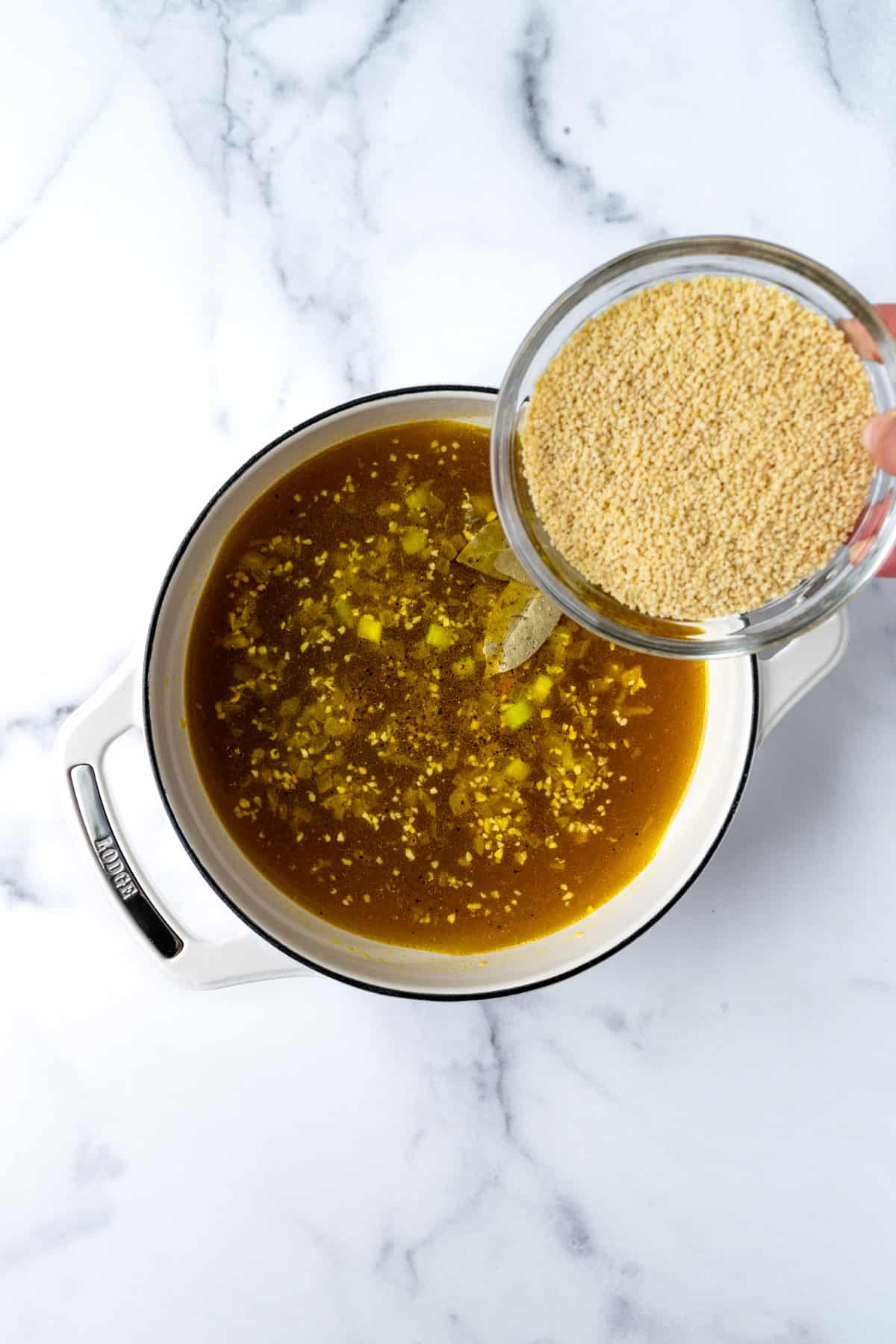 Adding pastina to a pot of chicken soup in a white dutch oven.