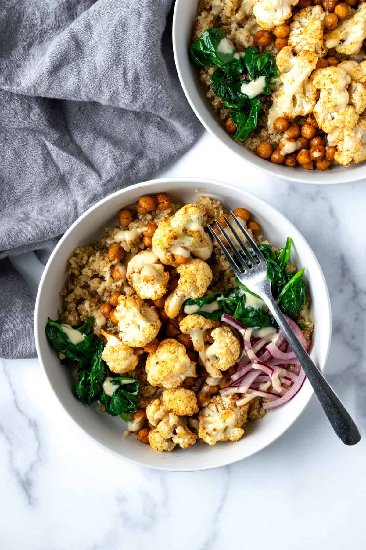 Roasted Cauliflower and Chickpeas in a white bowl with quinoa, spinach, and pickled onions.