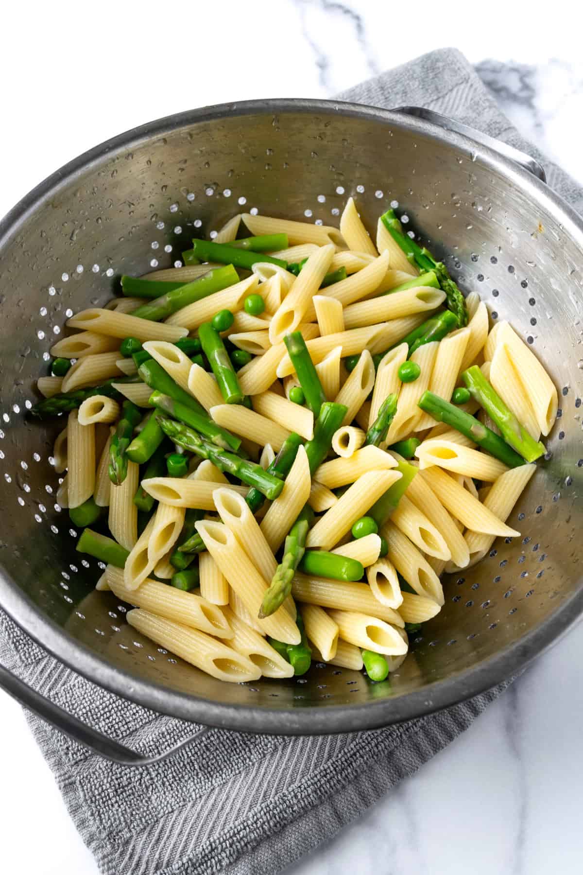 Cooked Pasta, Peas, and Asparagus in a colander.