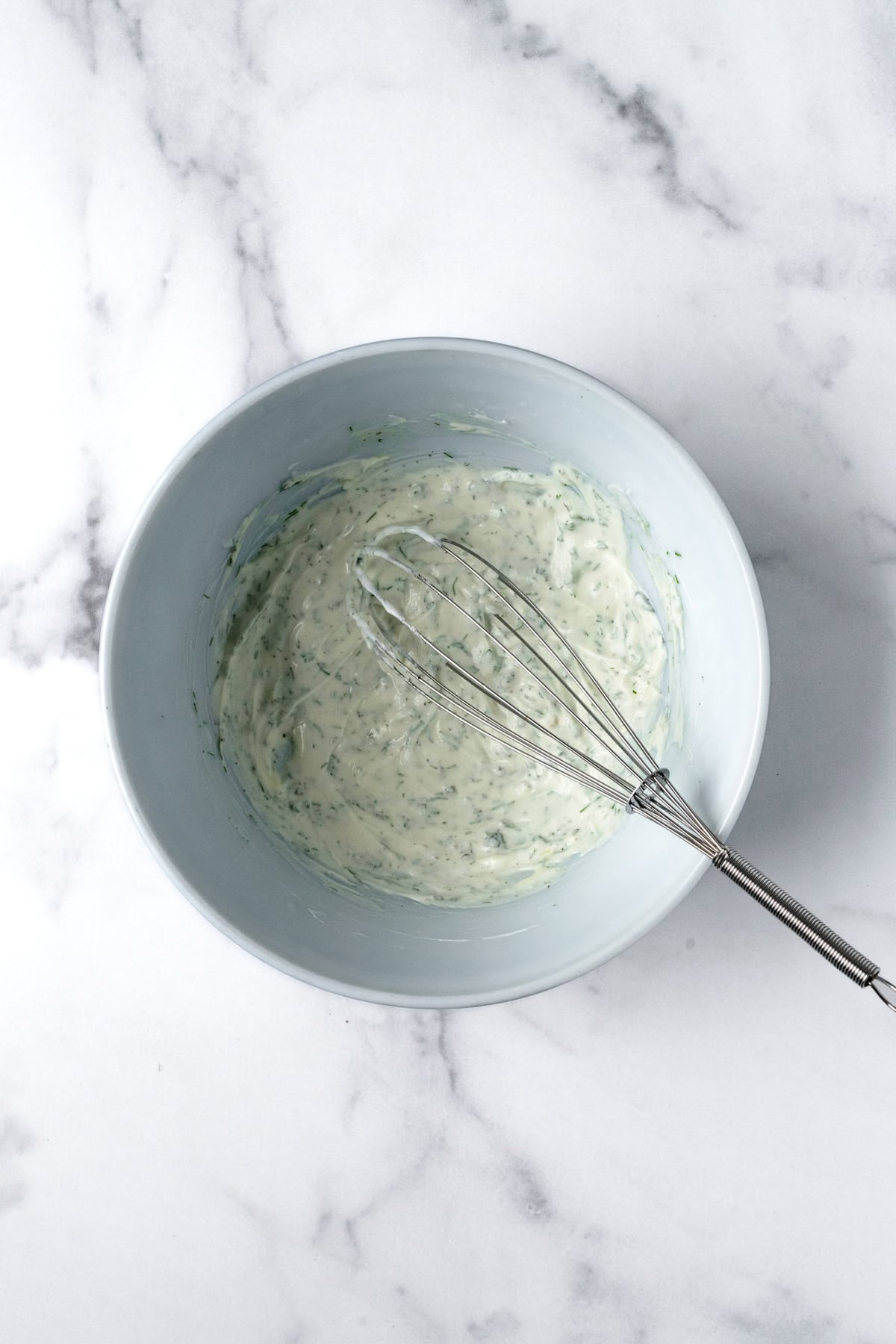 Greek Yogurt Dressing in a white bowl with a whisk.