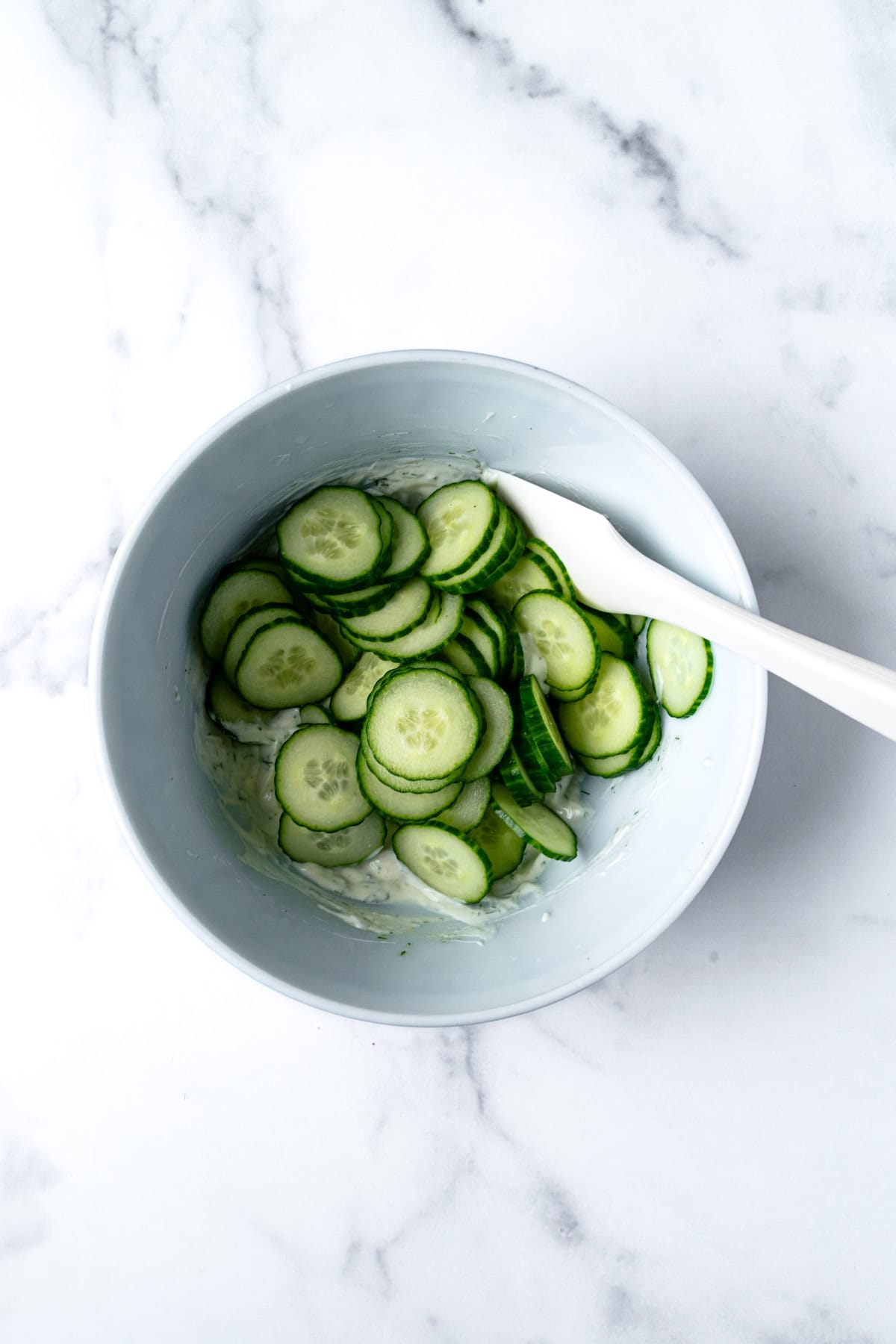Creamy Dressing and Cucumbers in Bowl with Silicone Spatula.