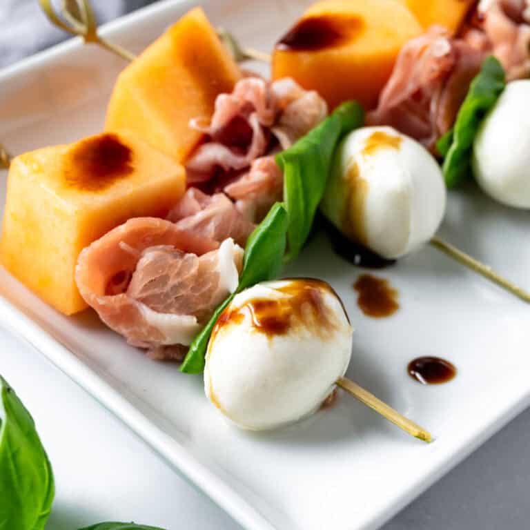 Prosciutto Melon Skewers with Balsamic Glaze on a white plate.