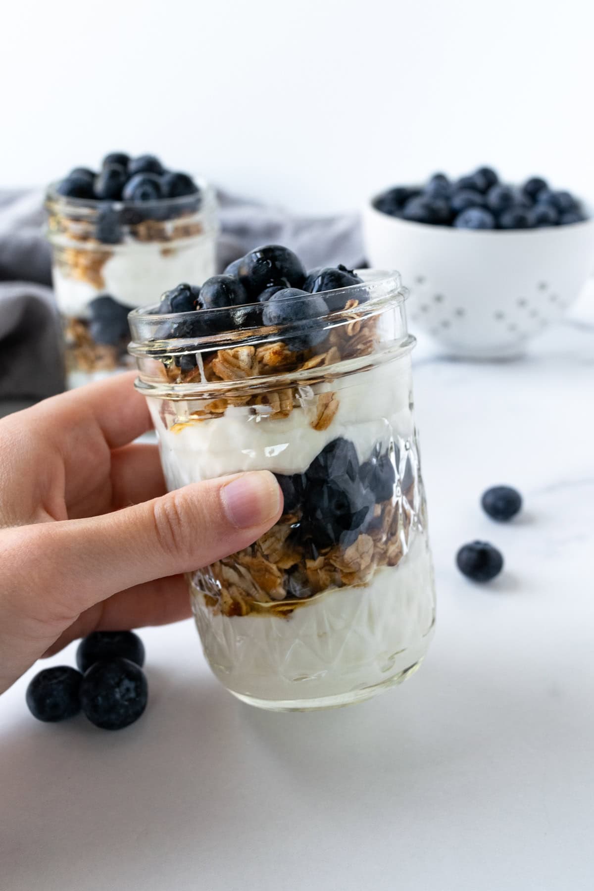 A hand holding a blueberry parfait in a glass jar.