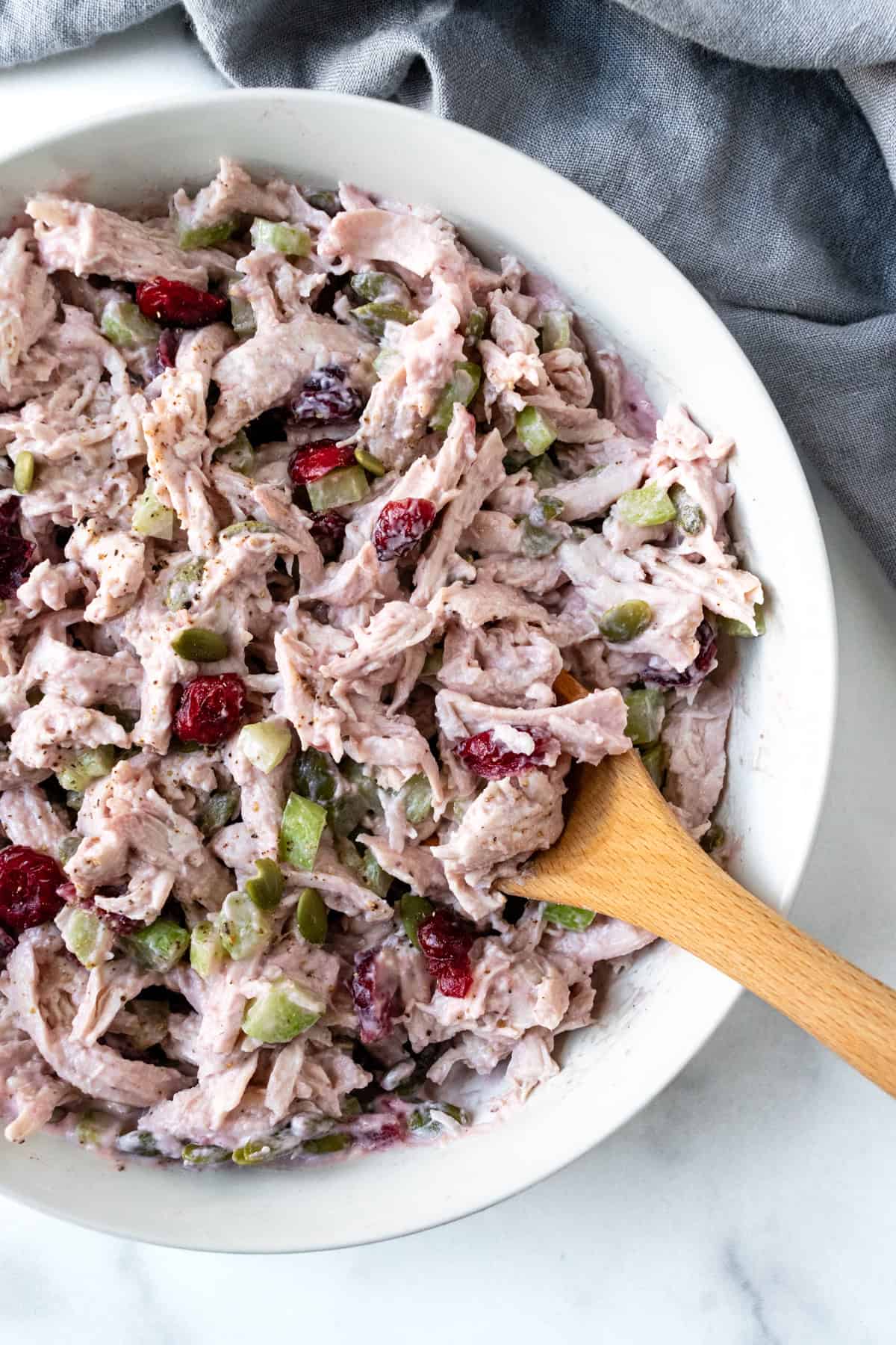 Cranberry Turkey Salad in a white bowl with a wooden spoon.