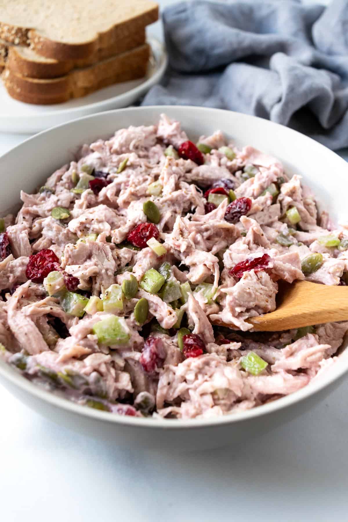 A scoop of Cranberry Turkey Salad on a wooden spoon from a white bowl.
