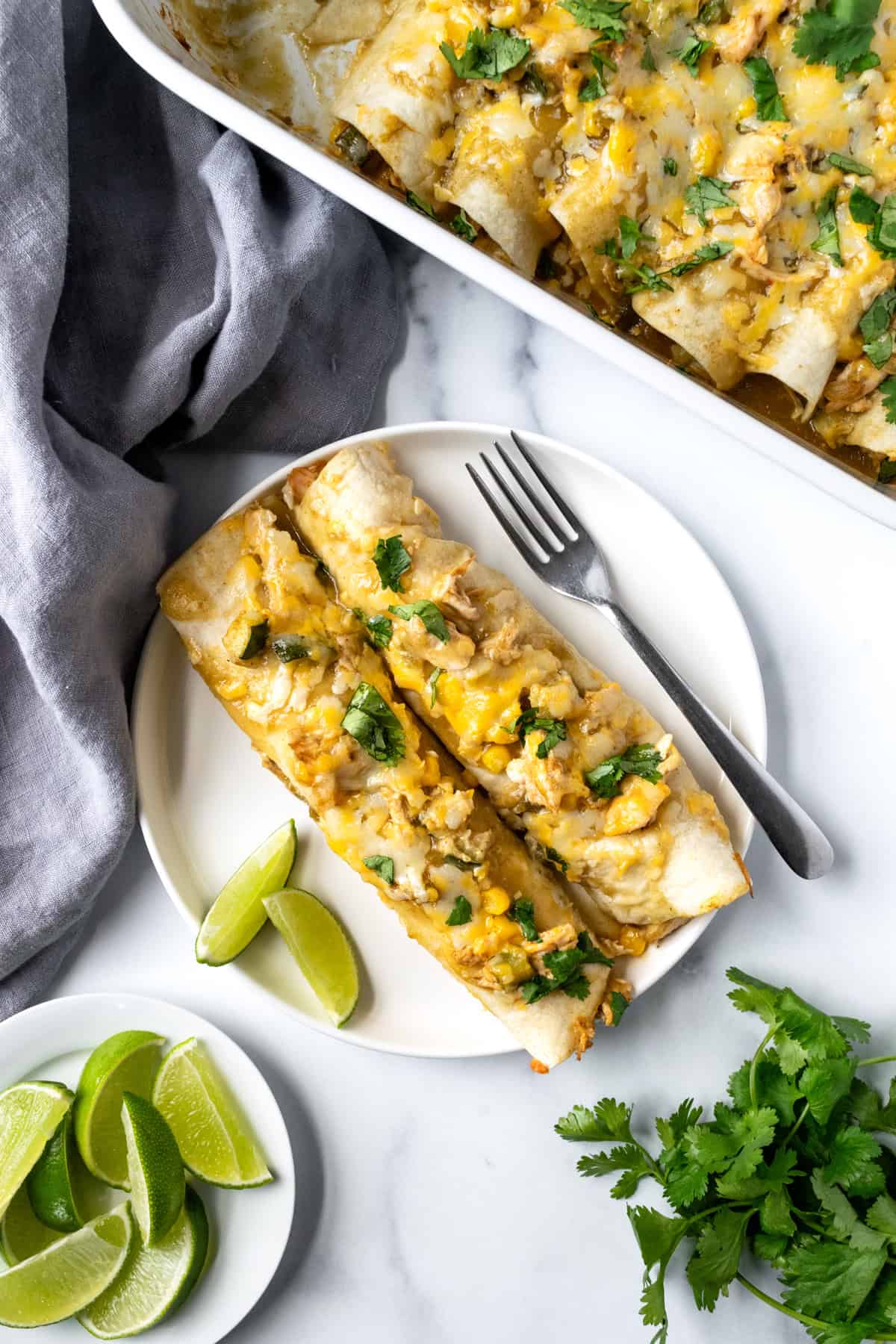 Chicken Enchiladas on a white plate with lime wedges for squeezing over it.