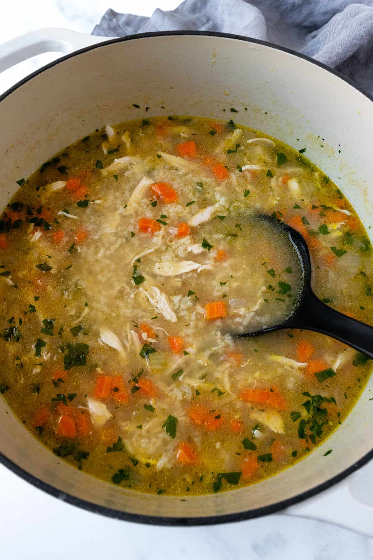 Ladle stirring lemon chicken and rice soup in a pot.