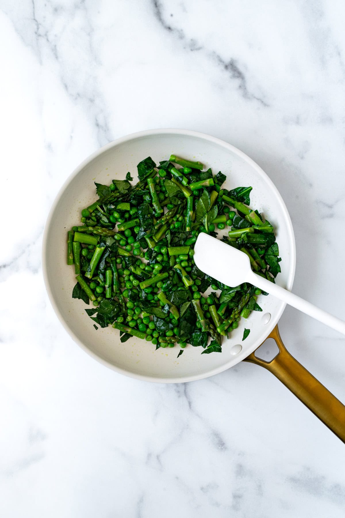 Sautéed spinach, peas, and asparagus in a white skillet.