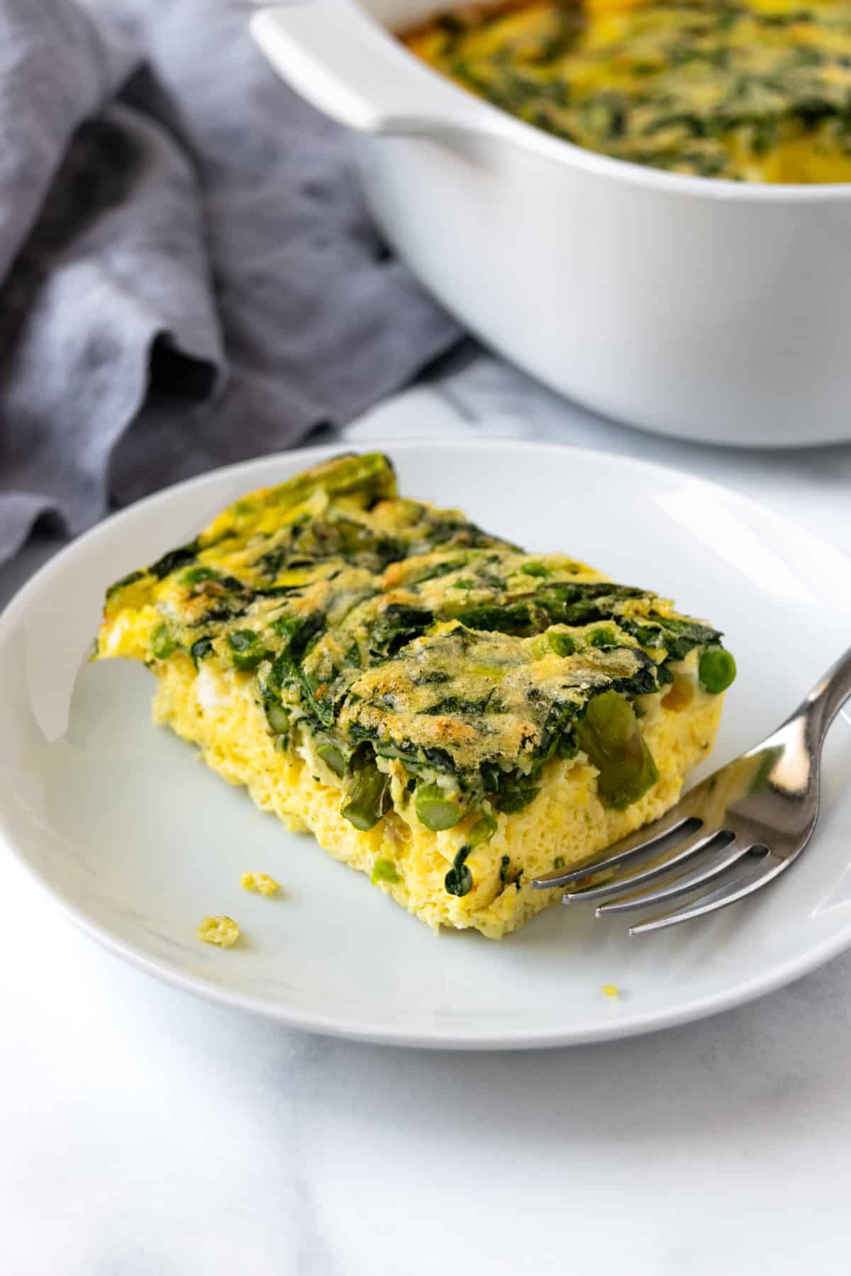 A slice of veggie egg bake on a white plate with a fork.