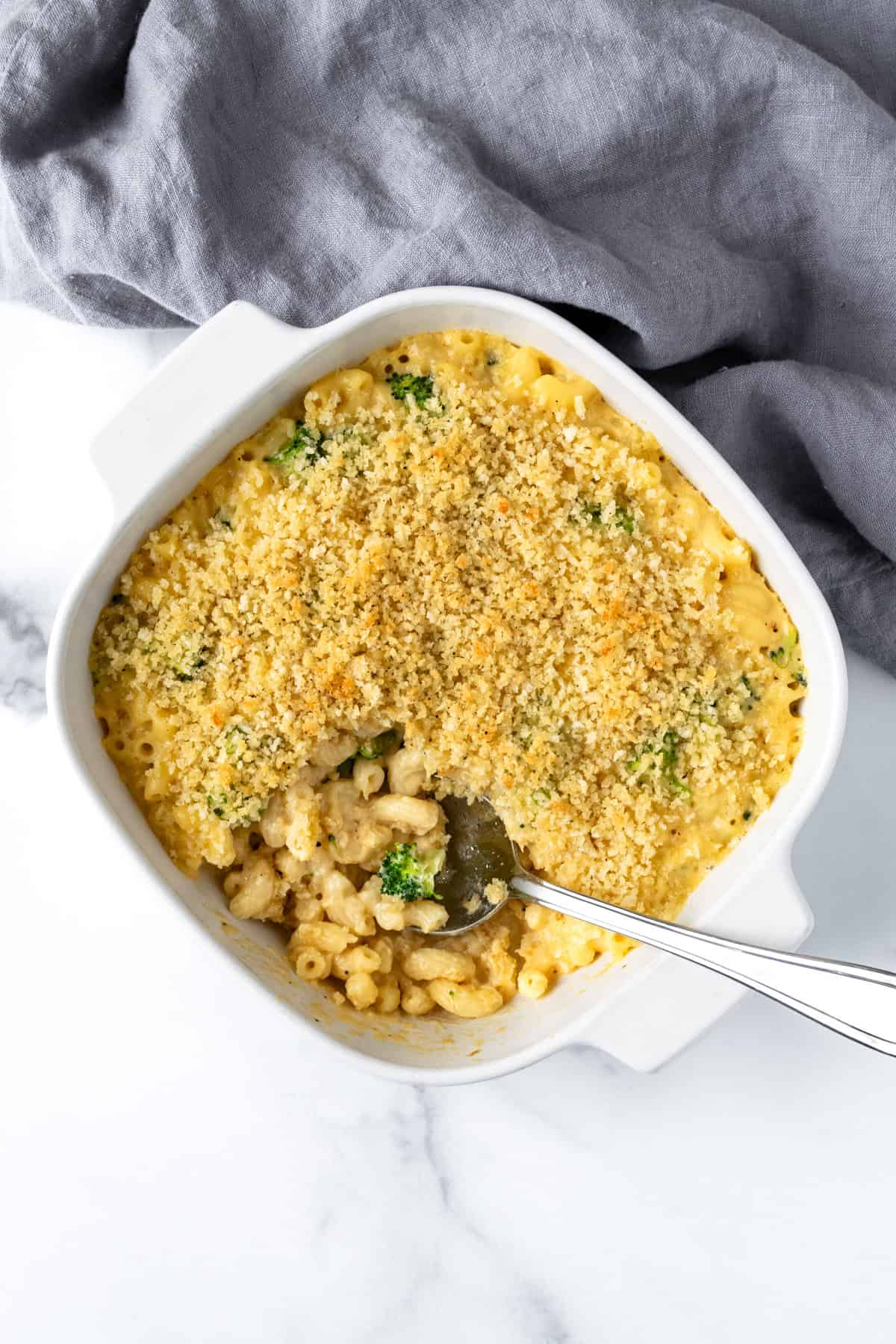 Baked Broccoli Macaroni and Cheese in a white casserole dish with a serving spoon.