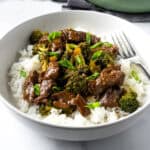 Beef and Broccoli served over rice in a white bowl with a fork.