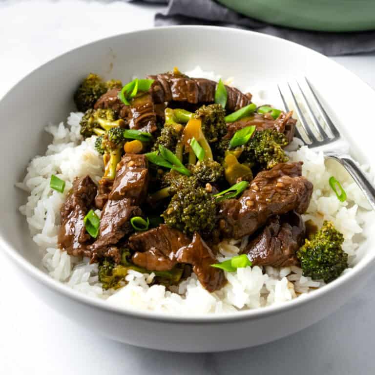 Beef and Broccoli served over rice in a white bowl with a fork.