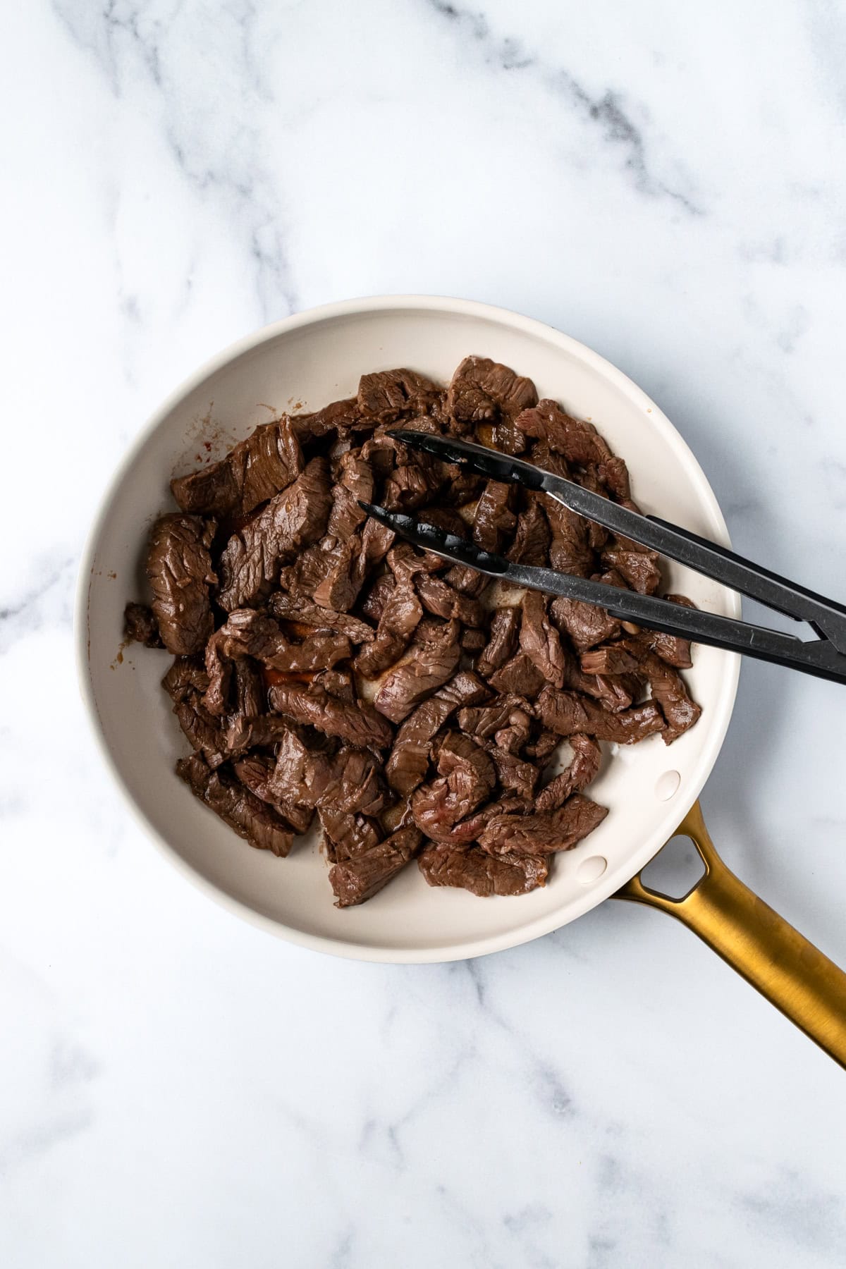 Cooked beef for beef and broccoli bowls in a white skillet.