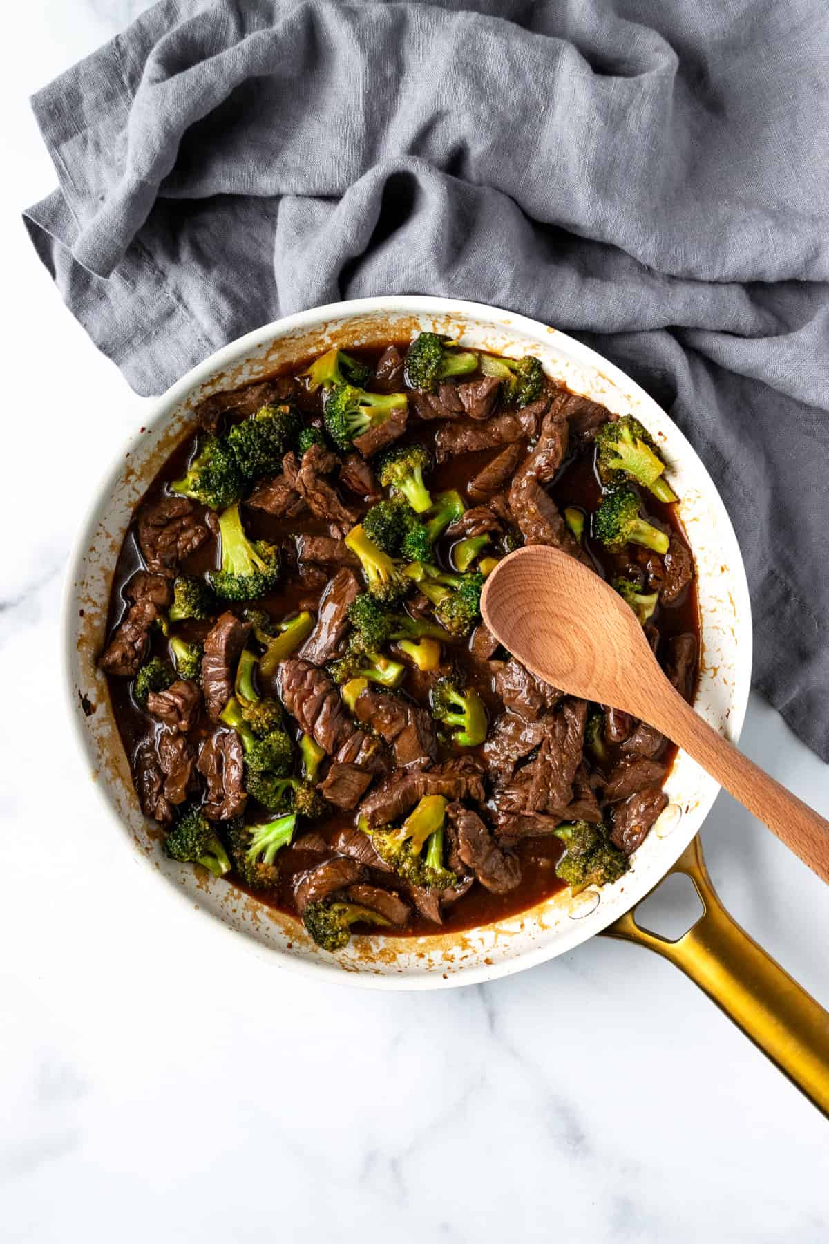 Beef and Broccoli in a white skillet with a serving spoon.